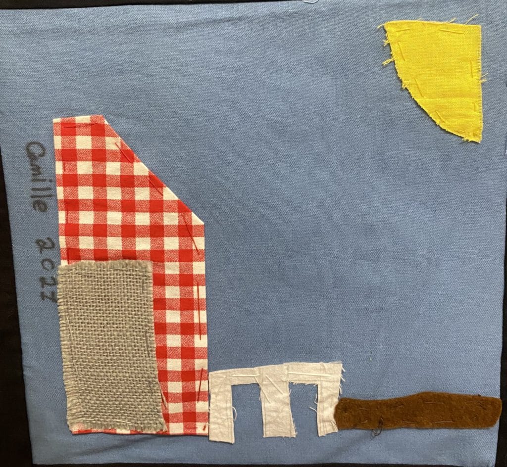 A blue square with a barn made of red and white checked fabric, with a yellow sun in the corner.