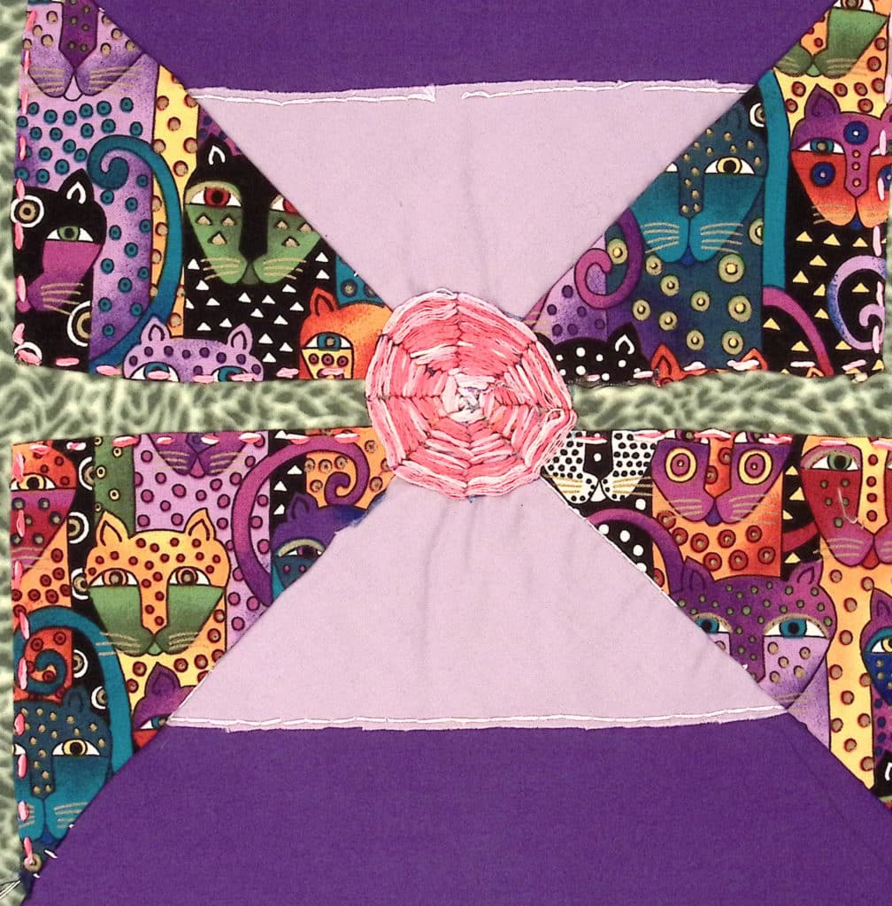 Lavender and purple background, with fabric depicting rainbow cats in triangles on the left and right sides, pink center.