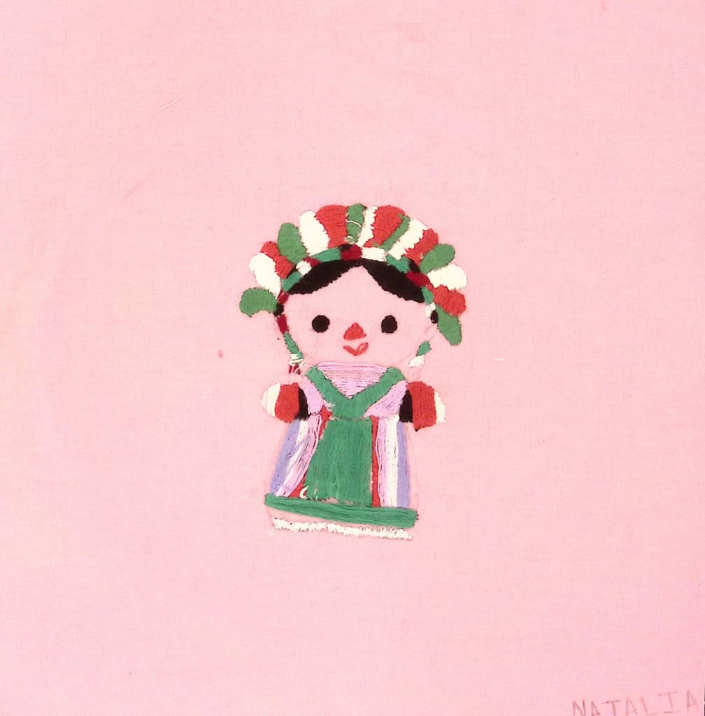 A pink square with an embroidered woman wearing traditional clothing in red, white and green.