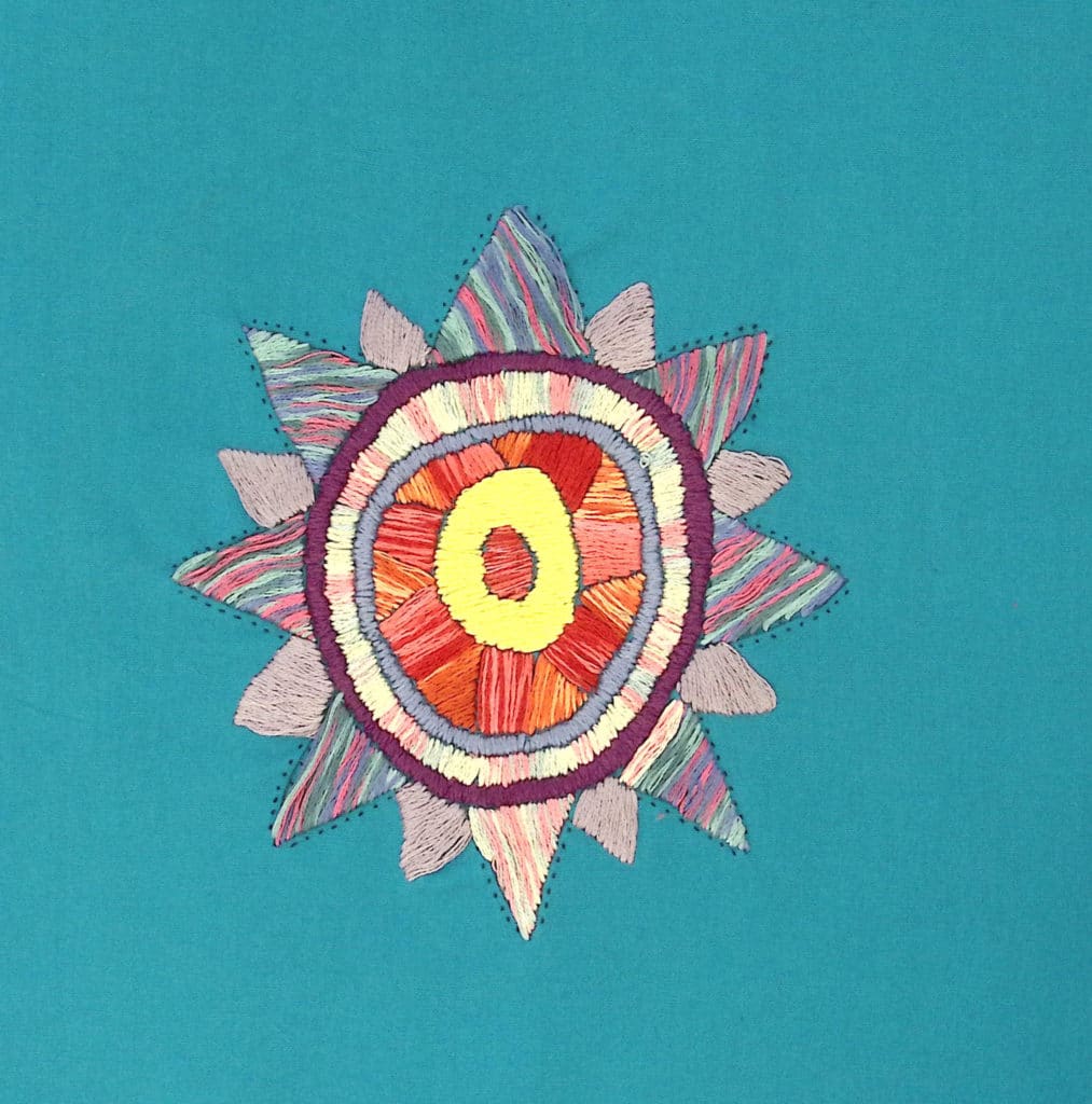 An embroidered purple and red sunburst on a red background.