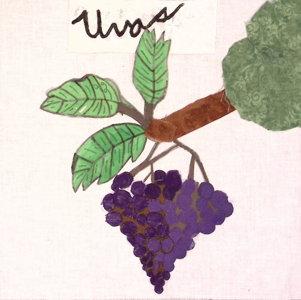 Large, purple grapes hang off of a leafy vine, with text above it reading "Uvas."