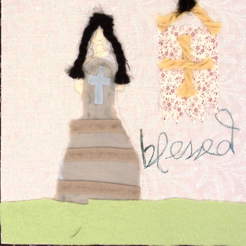 A woman with a long dress with a blue across on the chest and long dark hair, standing next to a floral square with a yellow cross on it, above text that reads, "blessed."