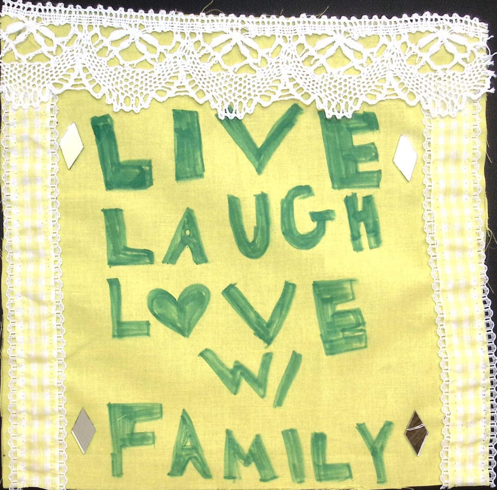 A yellow square with white lace borders, in green letters the words "Live laugh love with family."