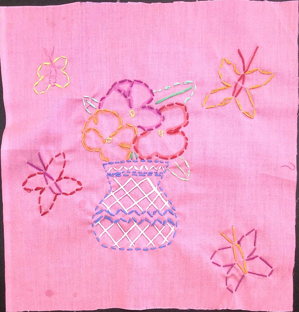 Embroidered flowers in a vase with butterflies on pink background