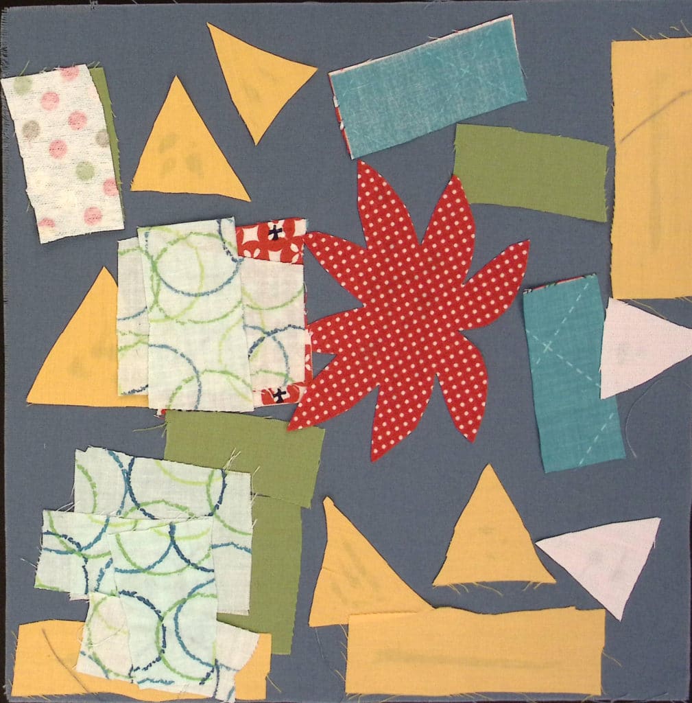A blue square with triangles and rectangles of yellow, blue and green fabric, a red leaf or flower in the center.