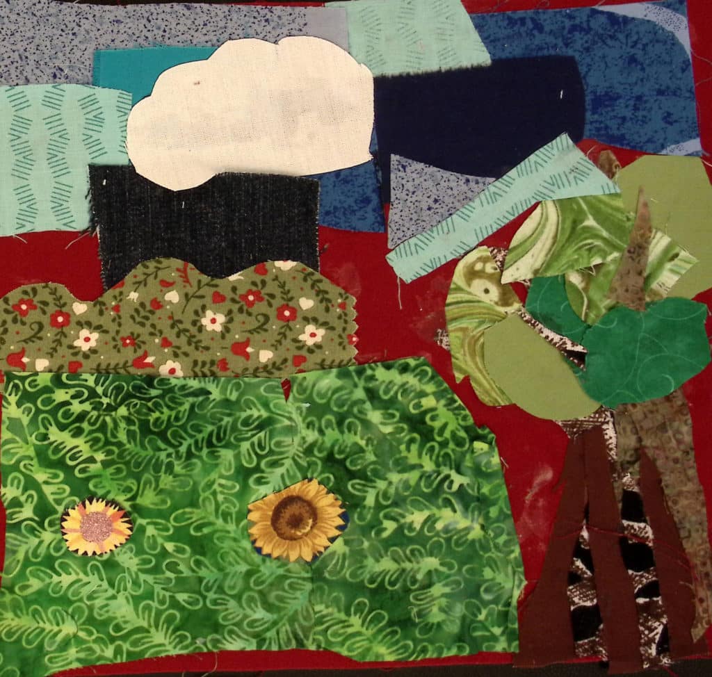 A tree, grass, and sky and clouds made with collage of fabric.