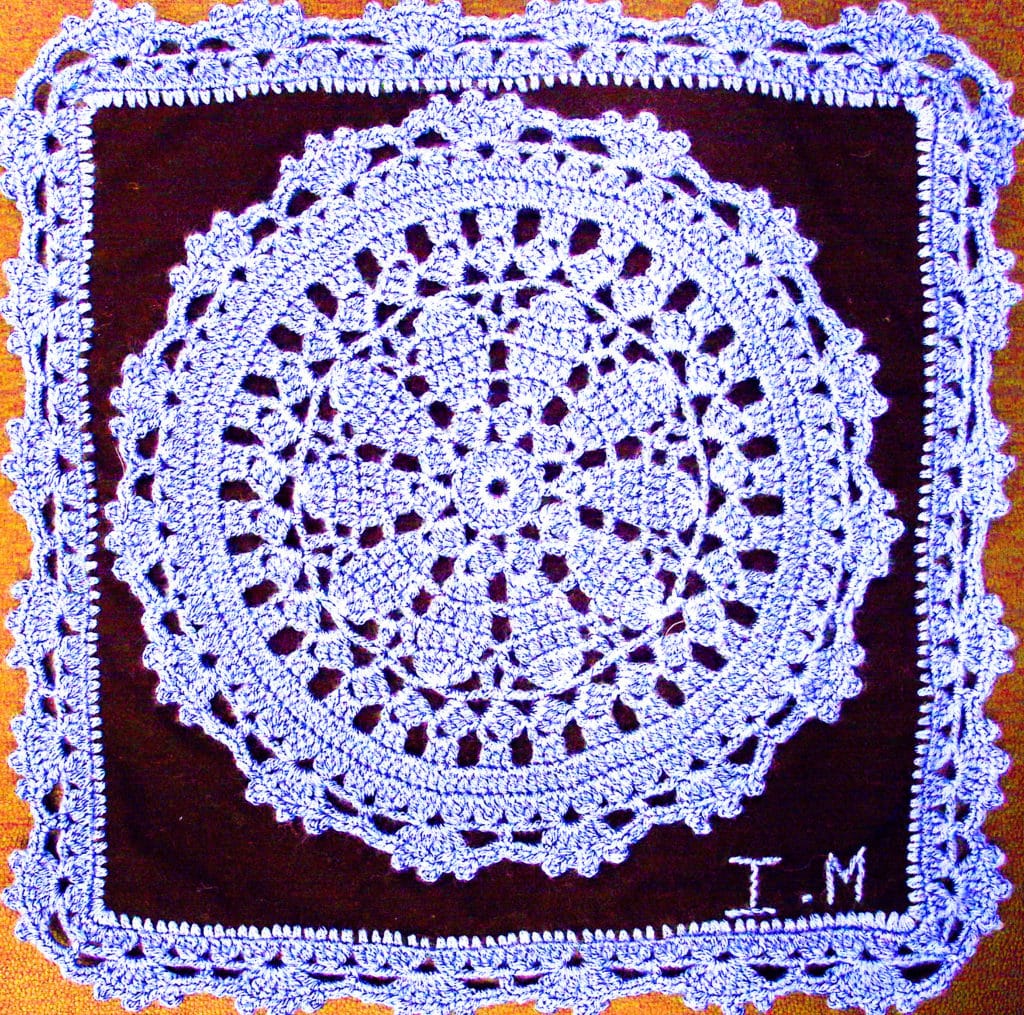 a blue crocheted doily attached to a black square, with blue crocheted edging.