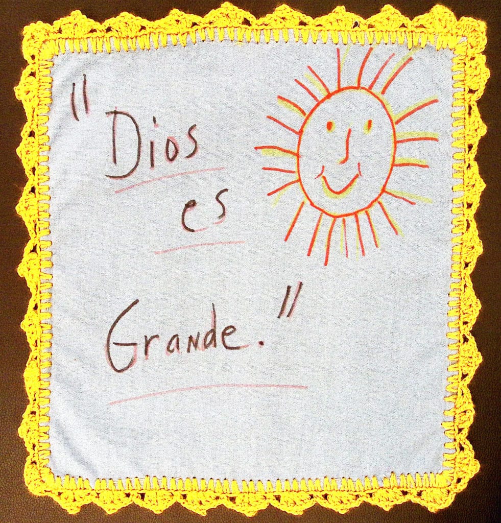 A smiling sun with the words "Dios es Grande" with a yellow crochet border