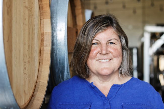 Photograph of Elaine St. Clair standing next to wine barrels