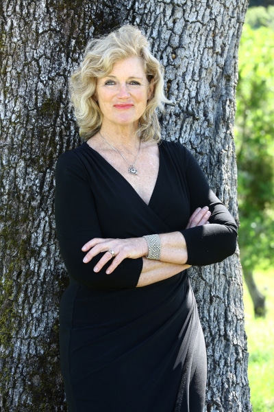 Photograph of Heidi Barrett in a black dress posing in front of a tree.