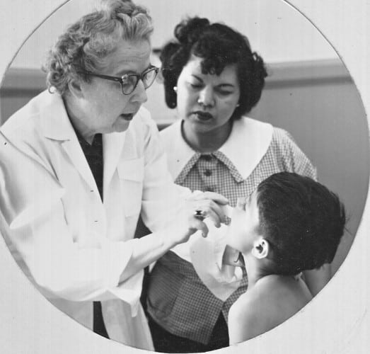 Dr. Ethel Priest examines a student while a young woman assistant observes.