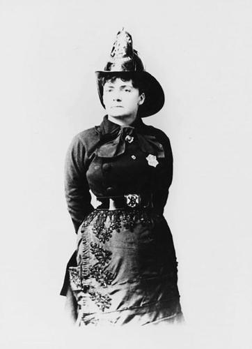 Lillie Hitchcock Coit posing wearing a tall Fireman's hat and a black top coat with a badge.