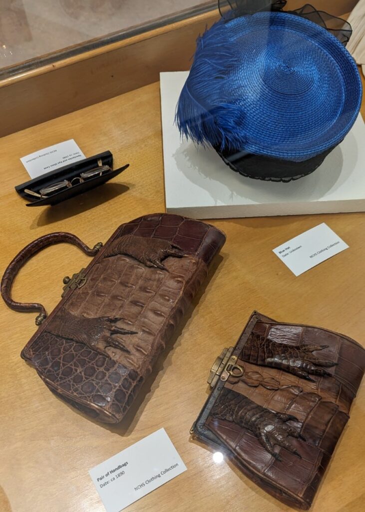 Various accessories including a blue woven hat circa 1950, two purses made from alligator leather, and a case with small spectacles. NCHS Clothing Collection.