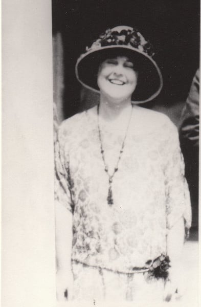 Rita Bordwell standing next to what appears to be a doorway wearing a brimmed hat and smiling.