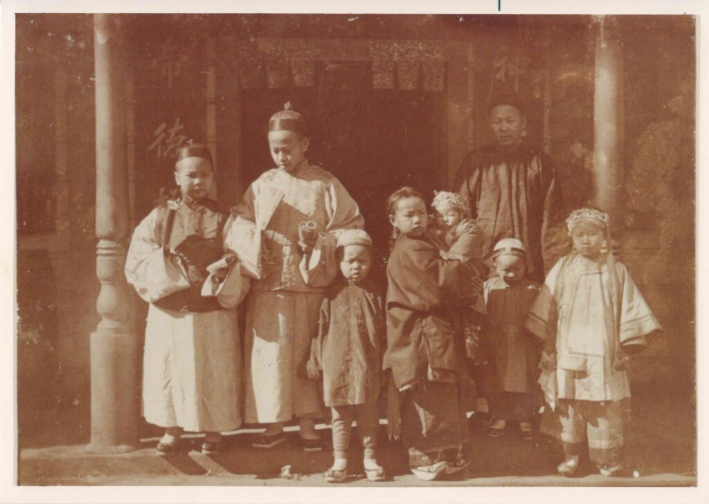 Chan Wah Jack and seven children standing in front of the Napa Chinatown Temple. The children are all dressed formally for Chinese New Year with the two oldest boys wearing matching robes and headbands.