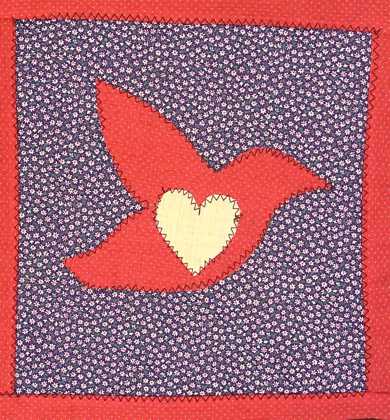 A quilted square featuring a red bird with a white heart in the middle.